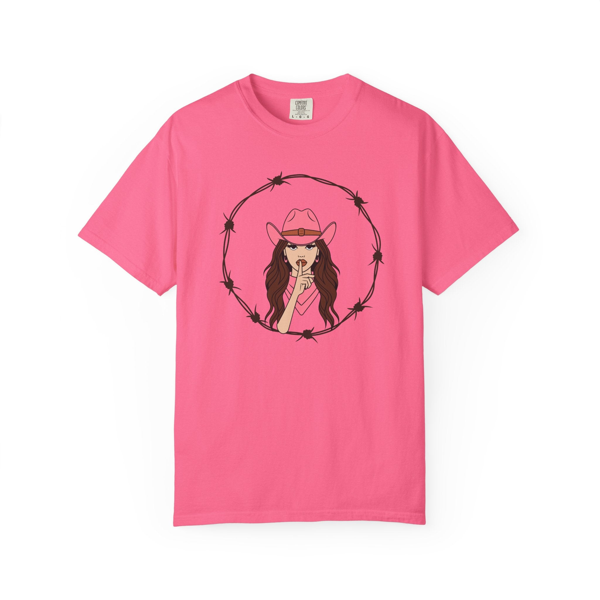 Pink t-shirt with illustrated woman in pink cowboy hat and top making a “shh” gesture, framed by a circular barbed wire border; bold Western graphic tee with edgy feminine flair