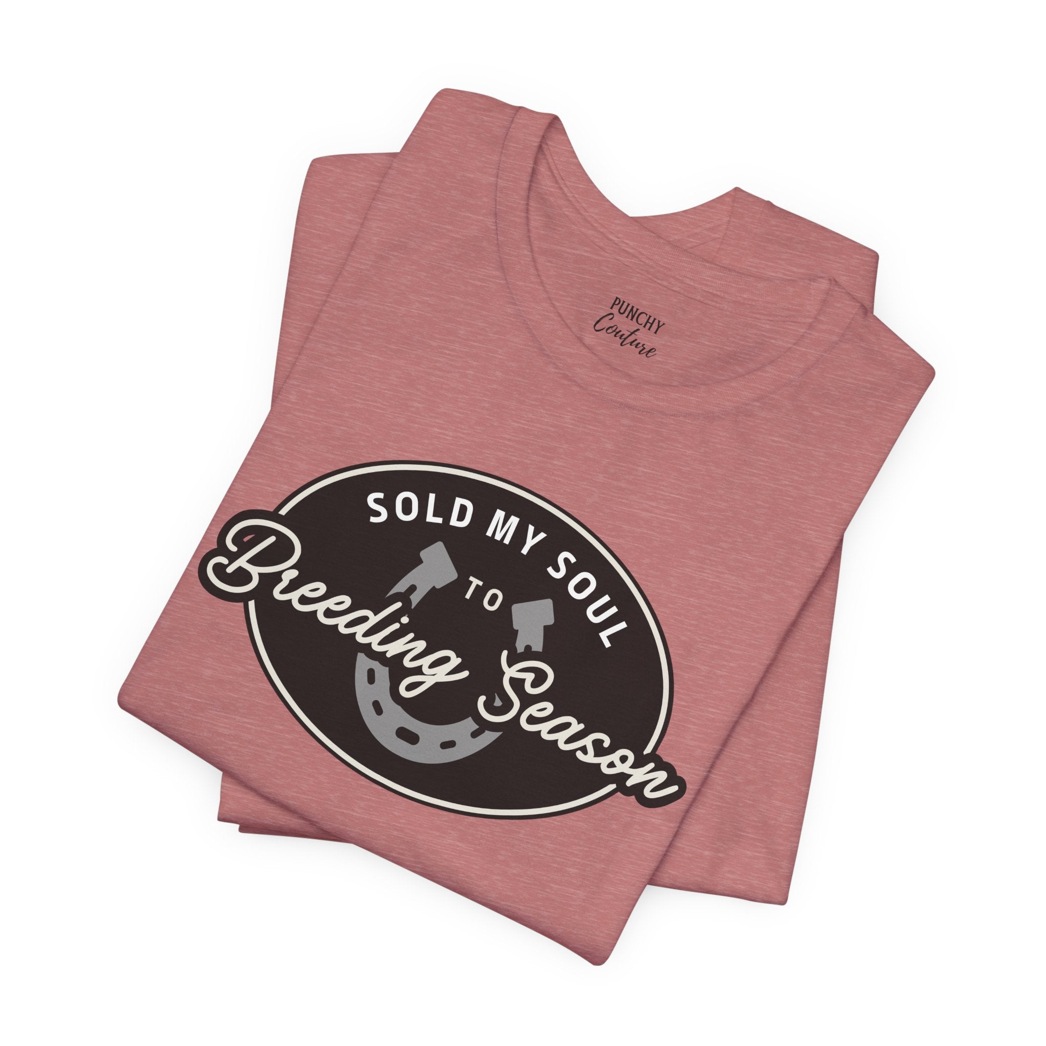 Folded pink t-shirt with black oval emblem featuring white text “SOLD MY SOUL TO Breeding Season” and horseshoe graphic; playful Western tee with ranch-ready attitude.