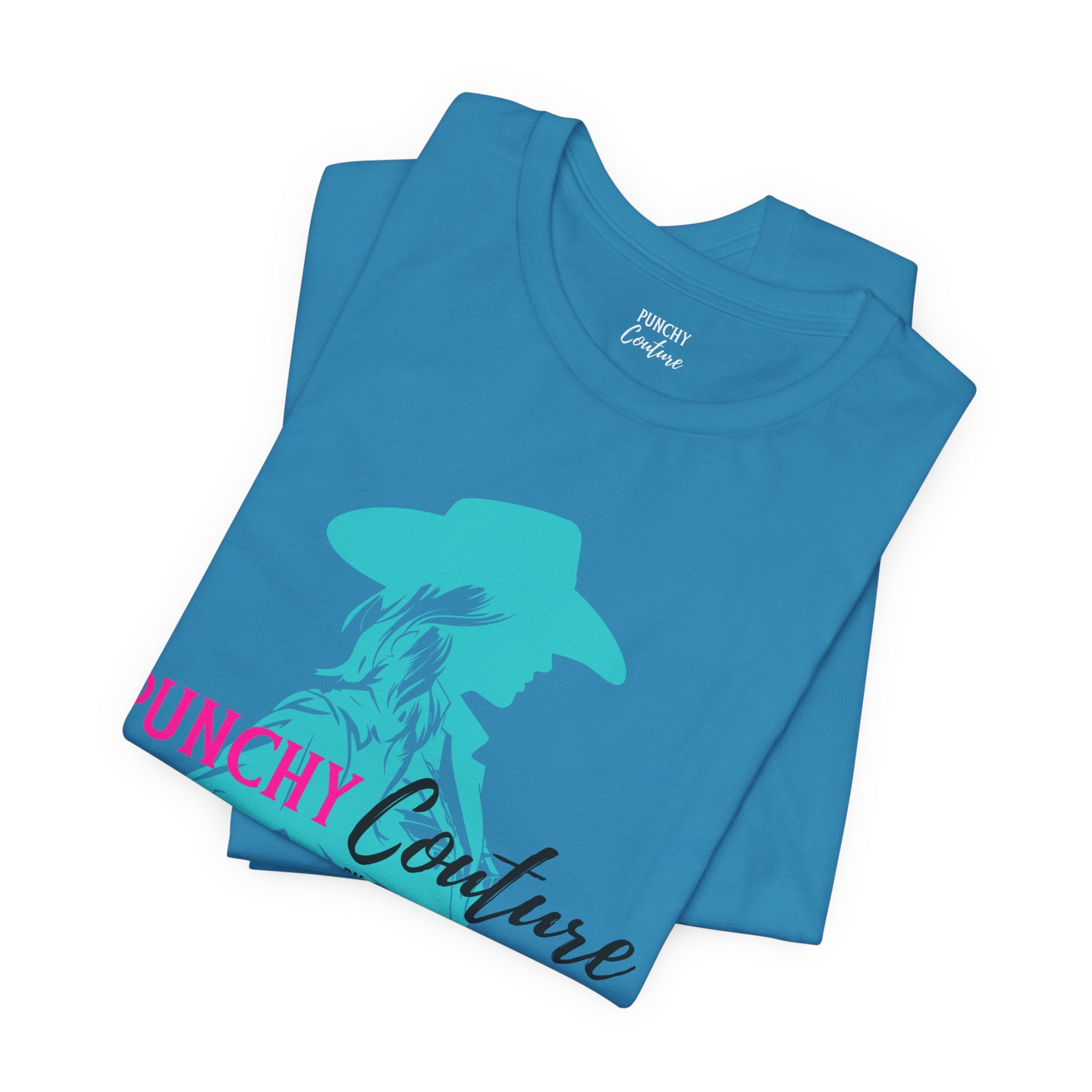 Blue t-shirt with turquoise cowgirl silhouette and bold pink "PUNCHY" text; features “Couture by Crazy Creative Cowgirl” tagline in black script and uppercase font; Western graphic tee with mythic brand energy.