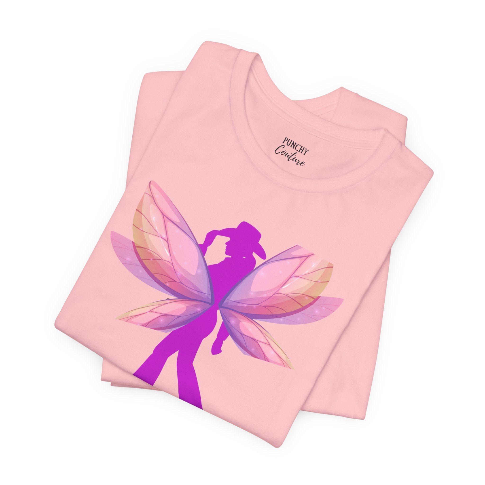 Light pink t-shirt with magenta cowgirl silhouette and layered fairy wings in pink, purple, and peach; whimsical Western graphic tee blending grit and enchantment.
