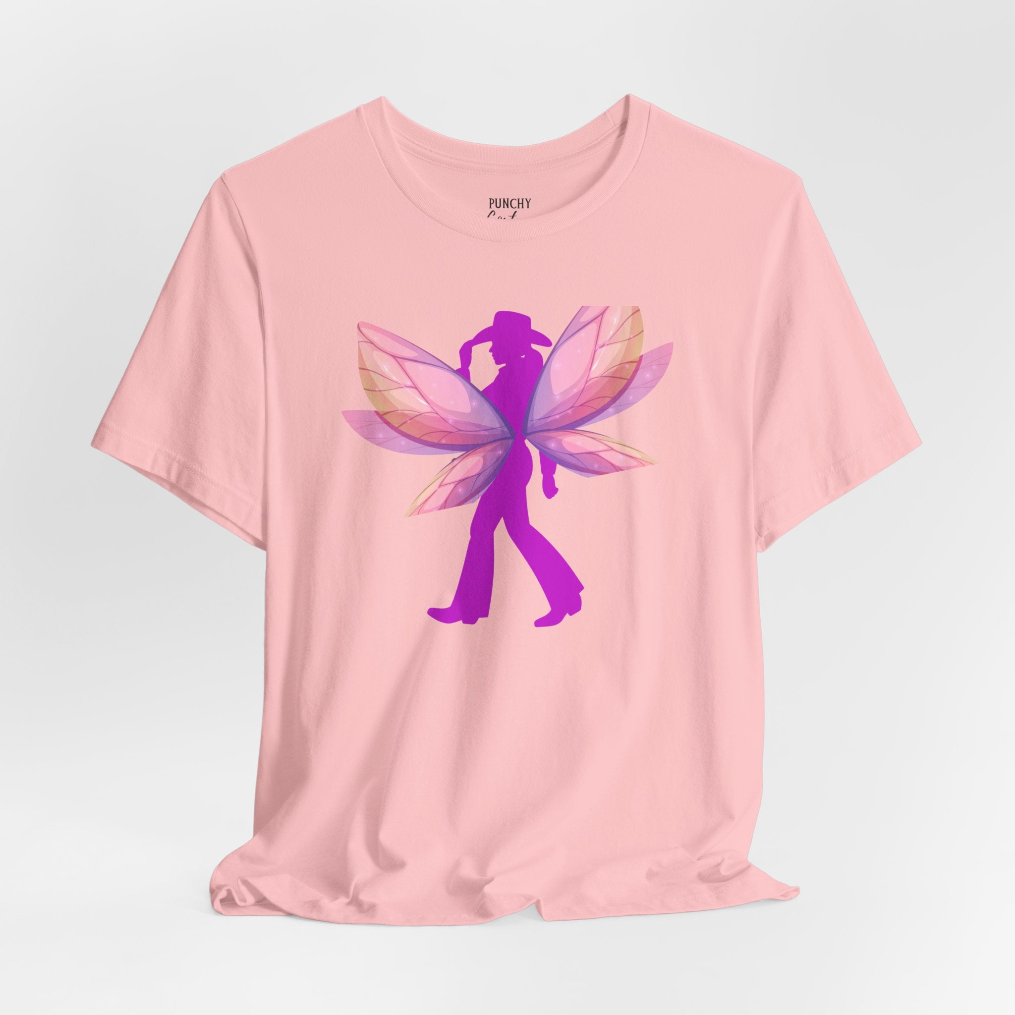 Light pink t-shirt with magenta cowgirl silhouette and layered fairy wings in pink, purple, and peach; whimsical Western graphic tee blending grit and enchantment.