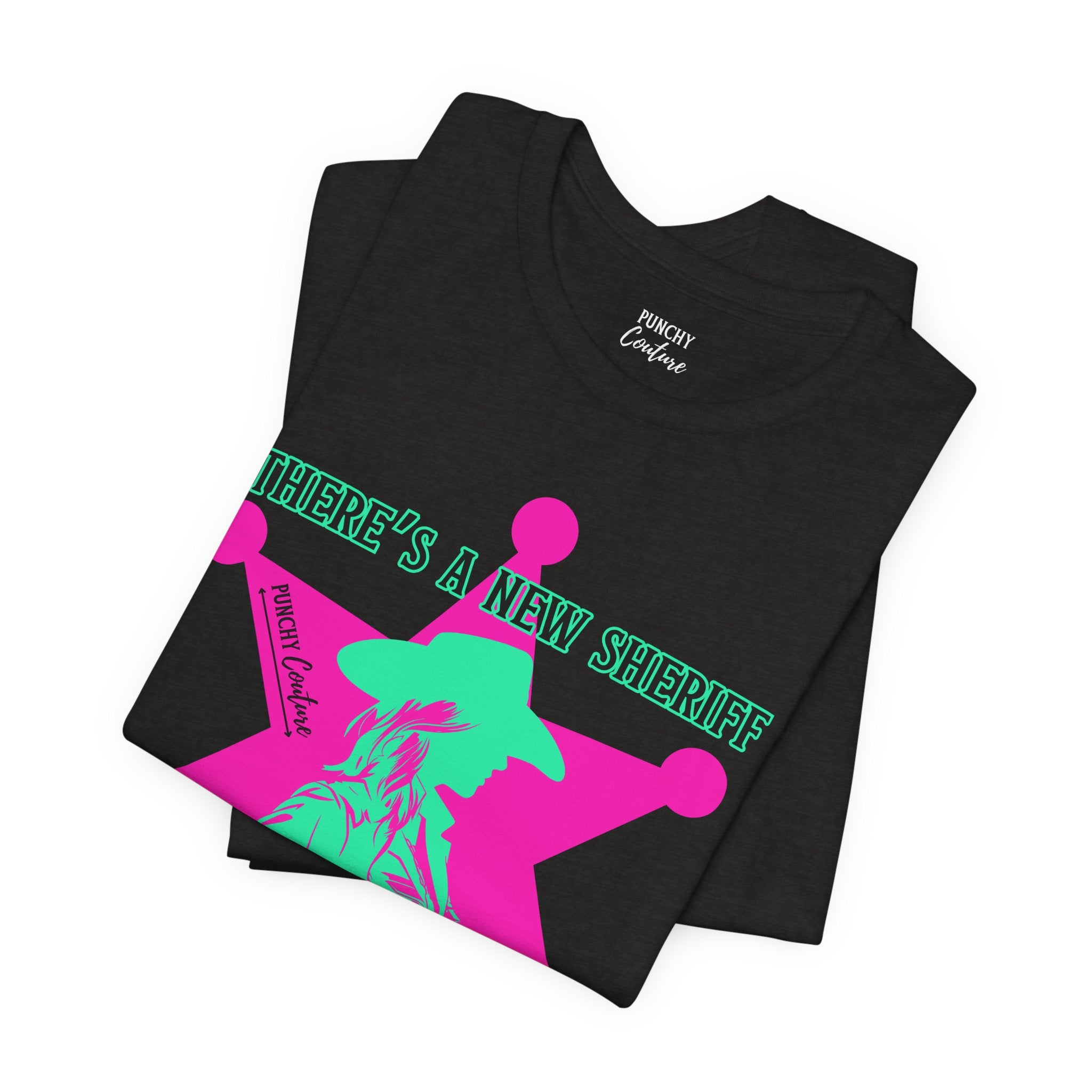 Black t-shirt with neon pink sheriff badge and green cowboy silhouette graphic; bold Western design featuring the phrase "THERE'S A NEW SHERIFF IN TOWN" and "PUNCHY COUTURE" branding.