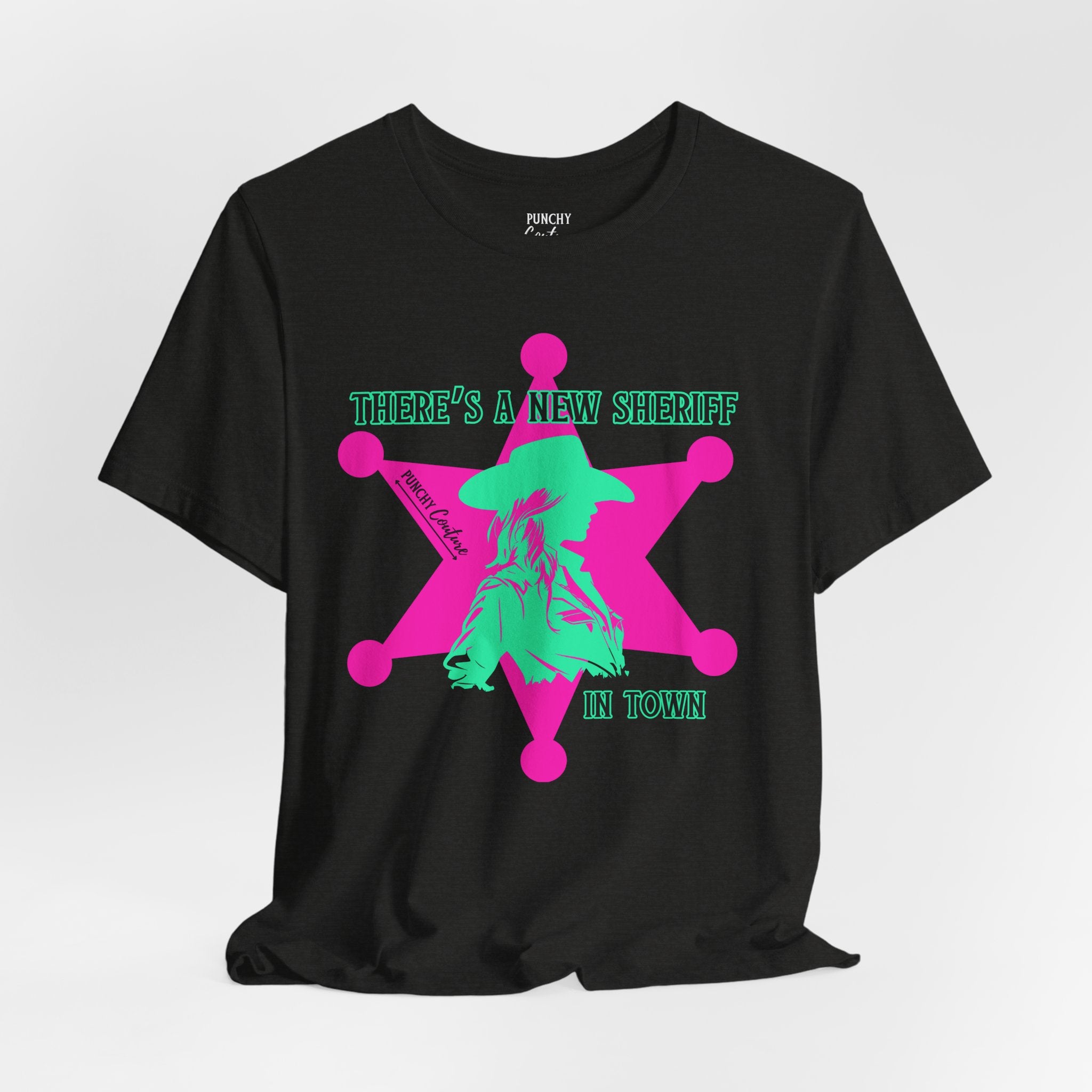 Black t-shirt with neon pink sheriff badge and green cowboy silhouette graphic; bold Western design featuring the phrase "THERE'S A NEW SHERIFF IN TOWN" and "PUNCHY COUTURE" branding.
