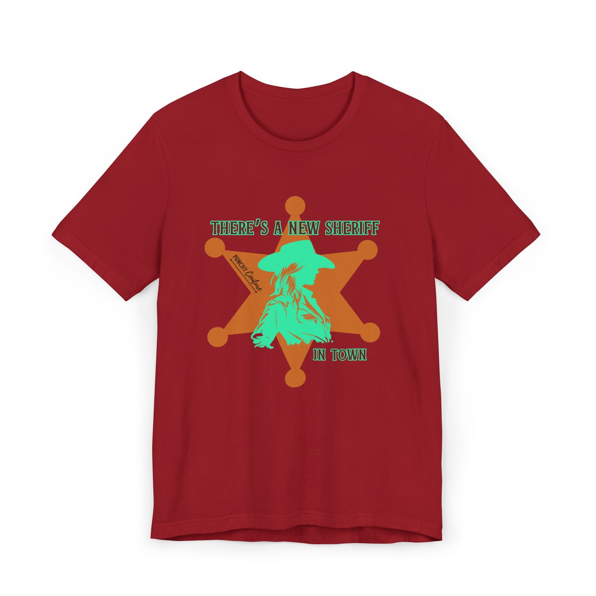Red t-shirt with orange sheriff badge and teal cowboy silhouette graphic; bold Western design featuring the phrase "THERE'S A NEW SHERIFF IN TOWN" and signature "Punchy Couture" text.