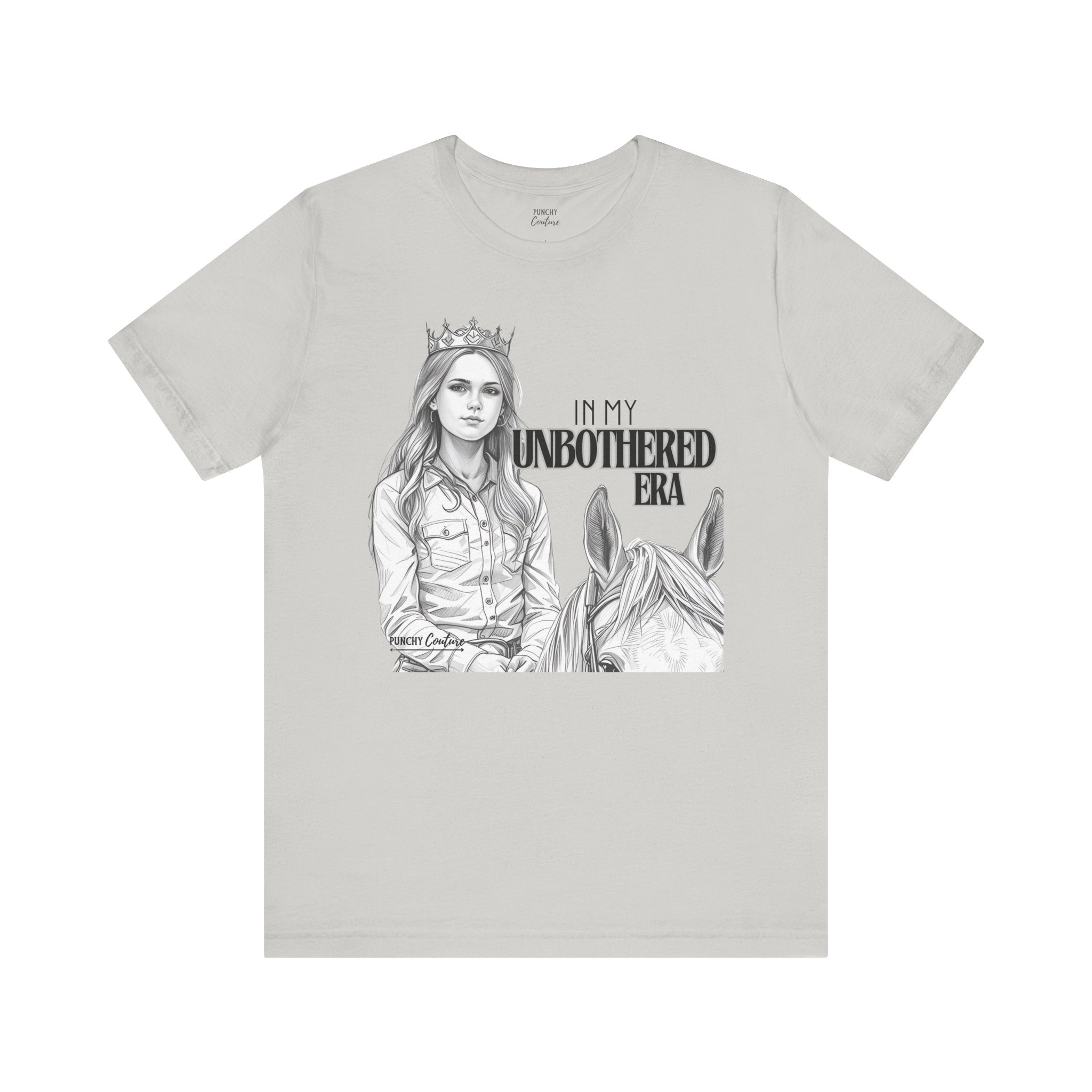 Light-colored t-shirt featuring a black-and-white illustration of a crowned cowgirl beside a horse, with bold text reading "IN MY UNBOTHERED ERA" and "PUNCHY COUTURE" below; a confident Western graphic tee celebrating sovereignty and style.