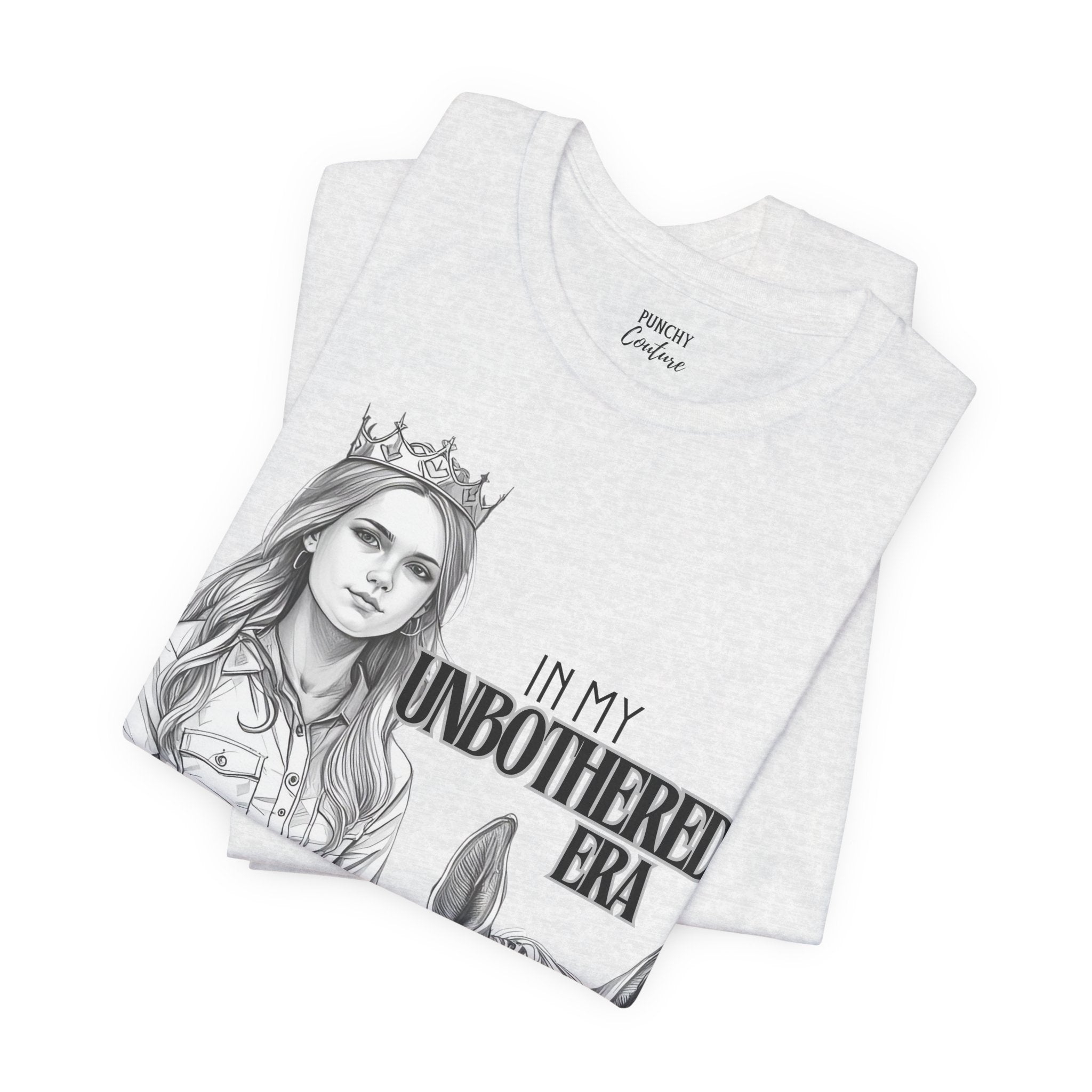 Light-colored t-shirt featuring a black-and-white illustration of a crowned cowgirl beside a horse, with bold text reading "IN MY UNBOTHERED ERA" and "PUNCHY COUTURE" below; a confident Western graphic tee celebrating sovereignty and style.